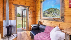 Een gezellig vakantiehuisje met houten inrichting, een open haard, een bank en een groot raam met uitzicht op de natuur.