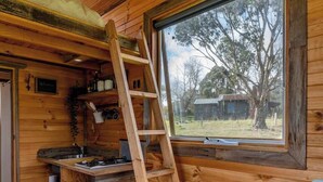 Een blokhutinterieur met houten inrichting, een raam met uitzicht, een houten trap en een keukenhoek.