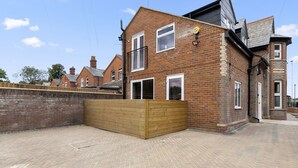 A brick house with a wooden fence, a paved driveway, and a clear sky. - Brand New Unique 2 Bedroom Apartment (Reading)
