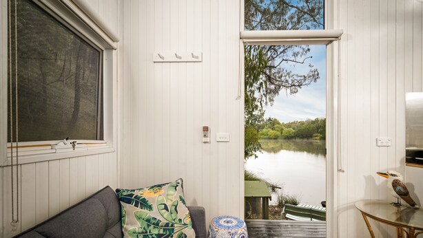 A room with a grey sofa, a patterned pillow, a round blue and white table, and a view of a lake with a boat.