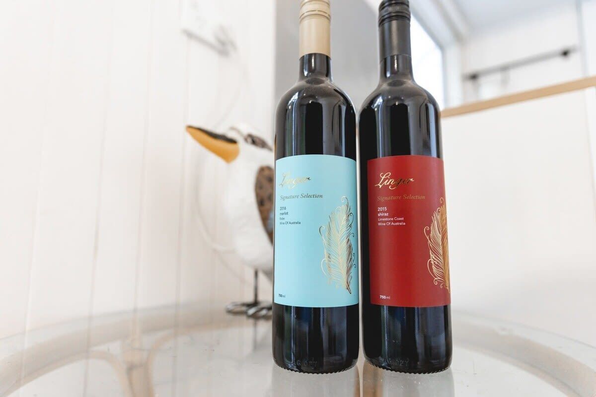 Deux bouteilles de vin sur une table en verre, avec un fond blanc et une sculpture d’oiseau.