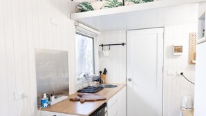 A compact kitchen with a wooden countertop, a sink, and a dishwasher. There is a window above the sink and a door to the right.