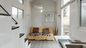 A compact room with a bed, a small table, a sink, and a window. - Raintree Farm Stay by Tiny Away (Sarsfield)