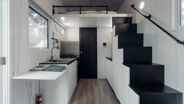 A compact kitchen with a white countertop, a black staircase, and a door leading to another room. - Raintree Farm Stay by Tiny Away (Sarsfield)