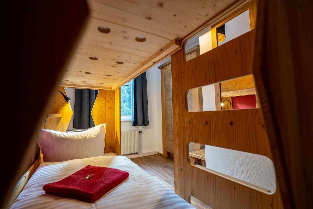 A wooden cabin room with a bed, a window, and a door with a mirror.