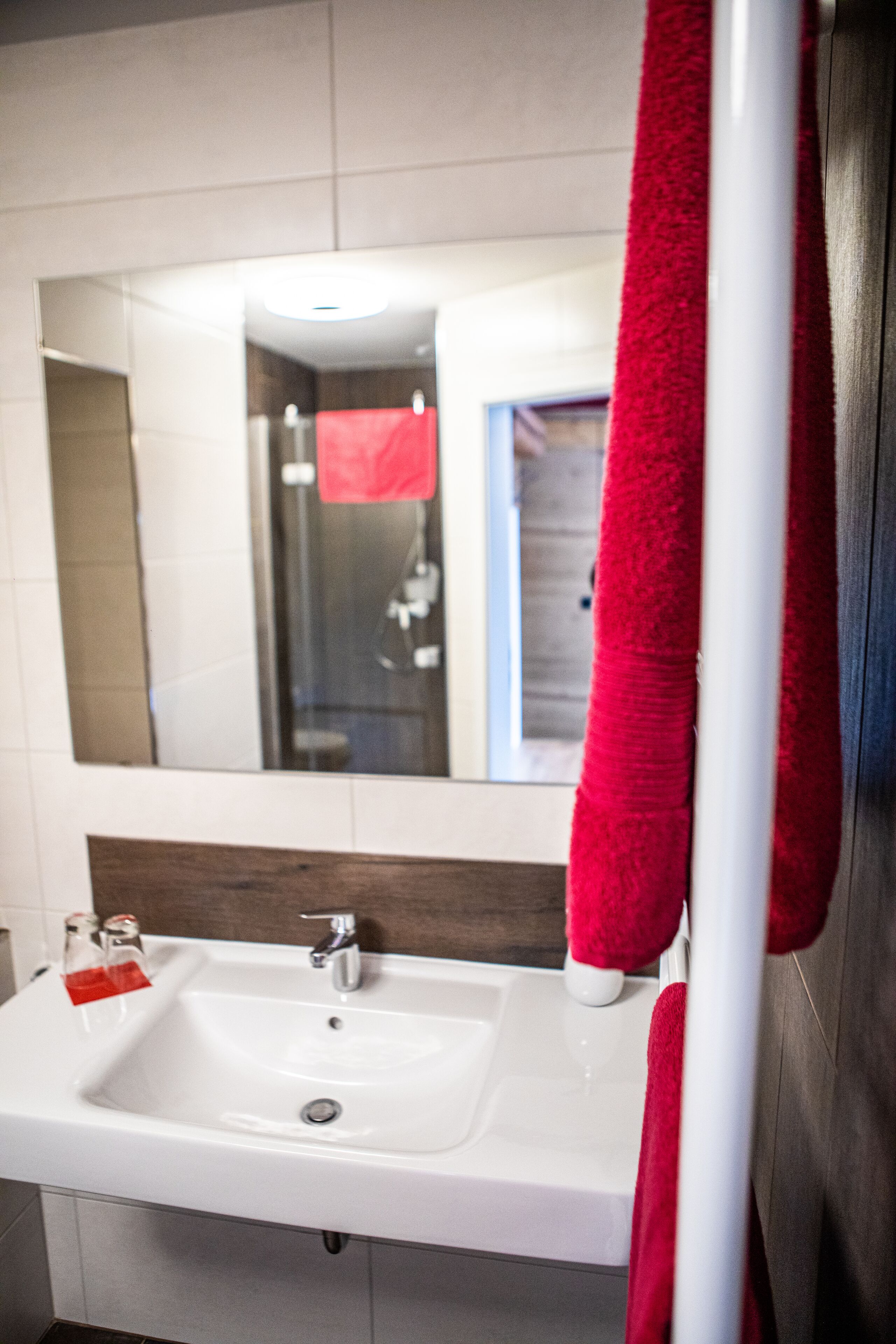 Une salle de bain avec un lavabo blanc, un miroir et une serviette rouge accrochée au mur.