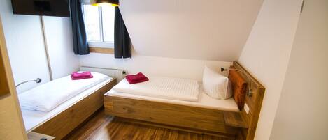 A small, compact room with a bed, a bedside table, a TV mounted on the wall, and a window with curtains.