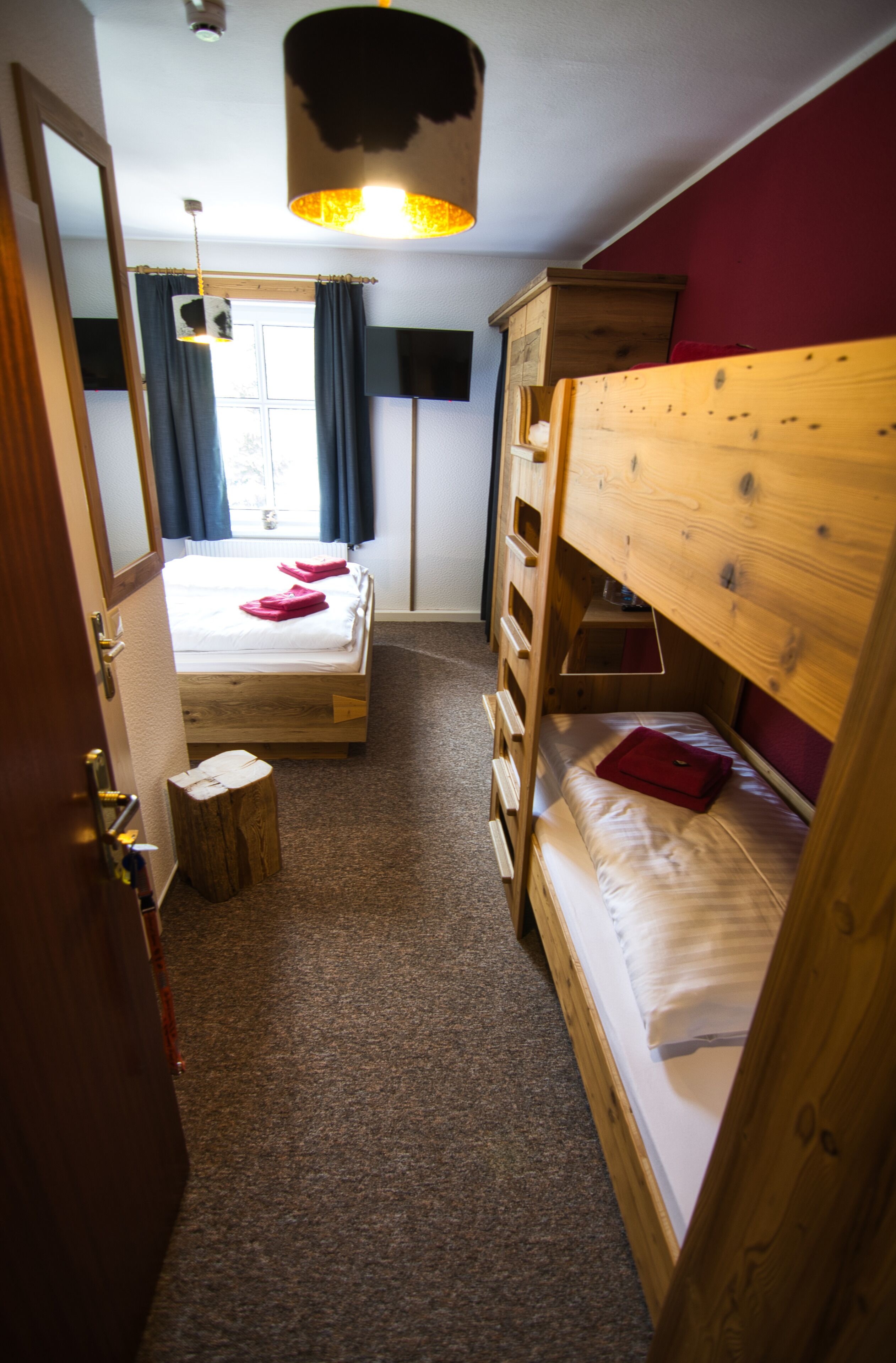 A room with a bunk bed, a wooden dresser, a small stool, and a window with curtains.