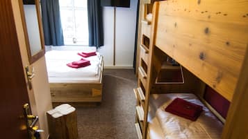 A room with a bunk bed, a wooden dresser, a small stool, and a window with curtains.