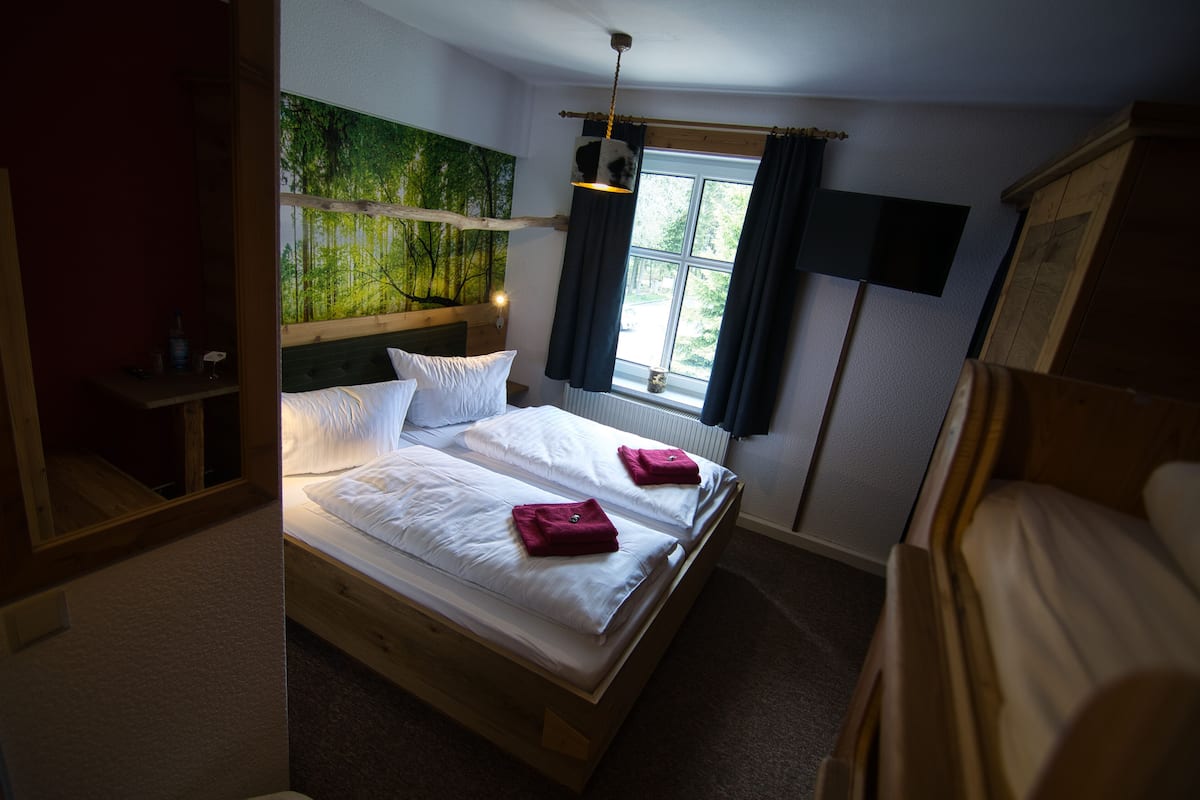 A bedroom with two beds, a wooden headboard, a window with curtains, and a wall-mounted TV.