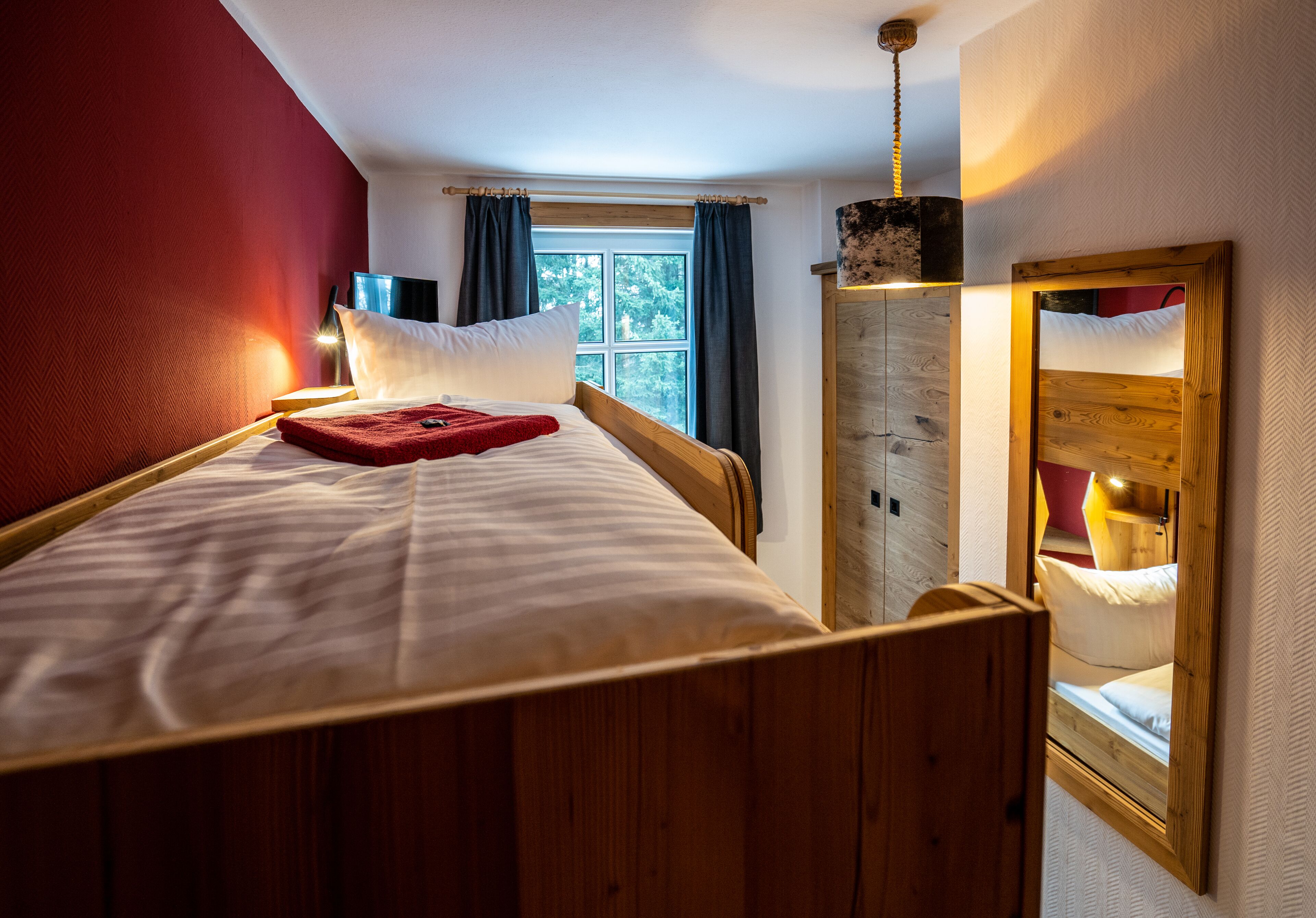 Una habitación con una cama de madera, una ventana con cortinas, un espejo y un armario de madera.