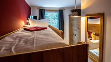 Una habitación con una cama de madera, una ventana con cortinas, un espejo y un armario de madera.