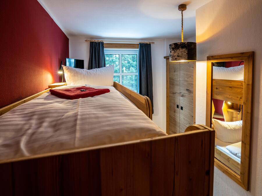 Una habitación con una cama de madera, una ventana con cortinas, un espejo y un armario de madera.