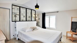Een moderne slaapkamer met een groot bed, een nachtkastje, een stoel, een raam met gordijnen en een spiegel bevestigd aan de muur.