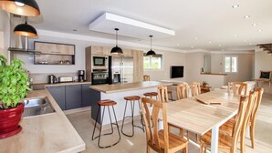 Een moderne keuken met een centraal eiland, barkrukken en een eettafel met stoelen.