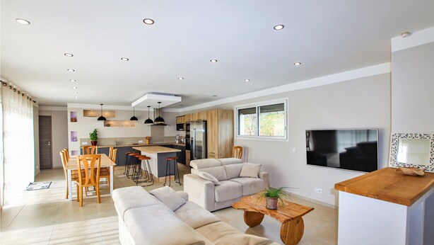 Een moderne woonkamer met een bank, salontafel en televisie. Er is een keuken met een eettafel en stoelen.