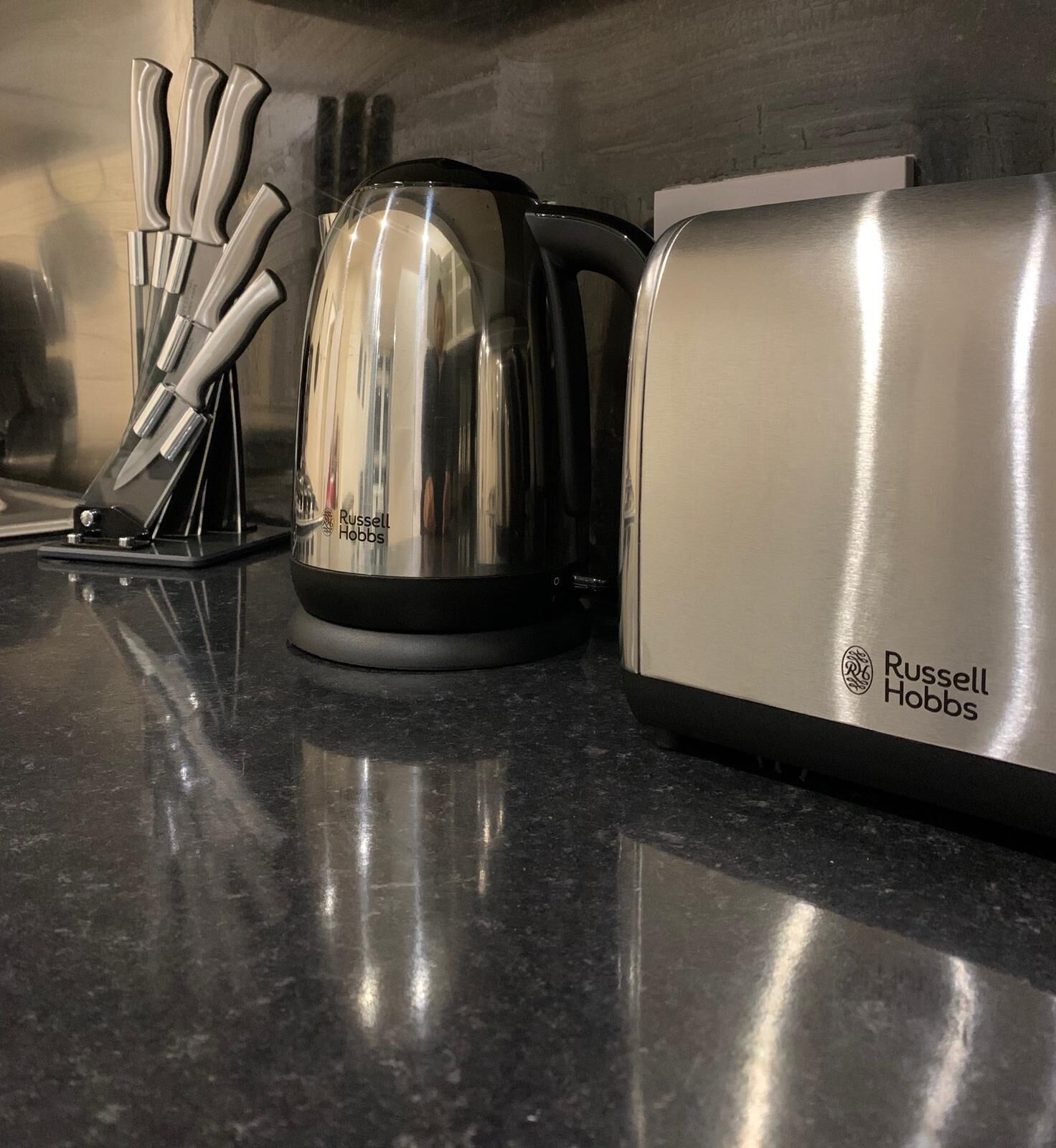 A kitchen counter with a kettle, a knife set, and a toaster.