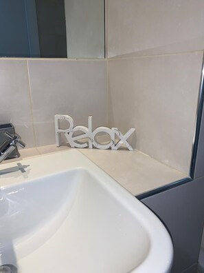 A bathroom with a white sink, a mirror, and a 'Relax' sign.