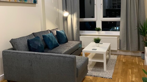 Ein modernes Wohnzimmer mit einem grauen Sofa, einem weißen Couchtisch und einem großen Fenster mit grauen Vorhängen.