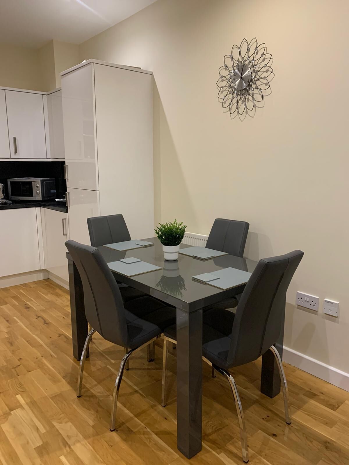 A modern kitchen with white cabinets, a microwave, and a dining table with four chairs.