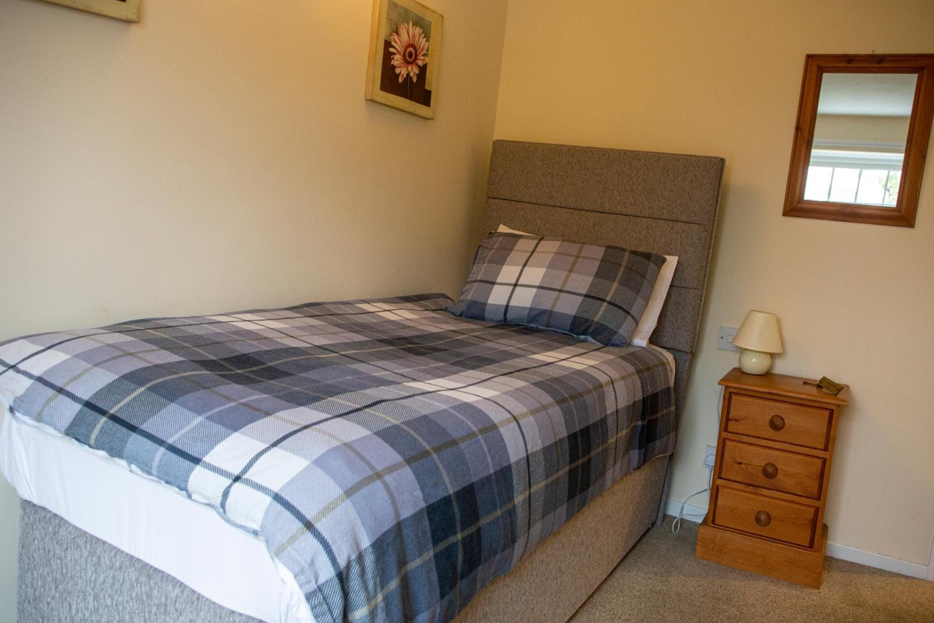 Une chambre à coucher comprenant un lit, une table de chevet, une lampe et un miroir fixé au mur.