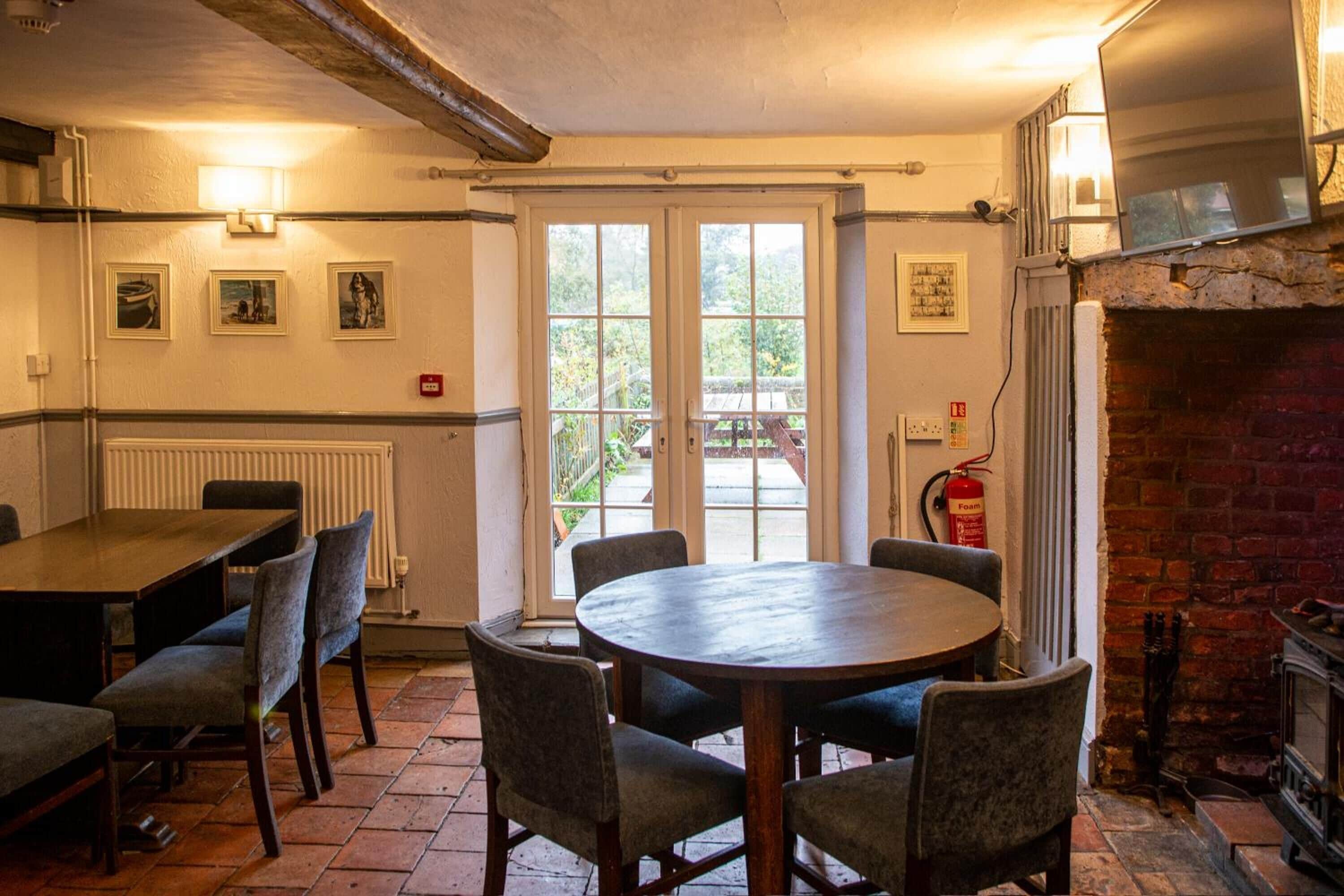 A dining area with a round table and chairs, a fireplace, and a view through a glass door to the outside.