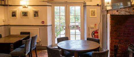 A dining area with a round table and chairs, a fireplace, and a view through a glass door to the outside.