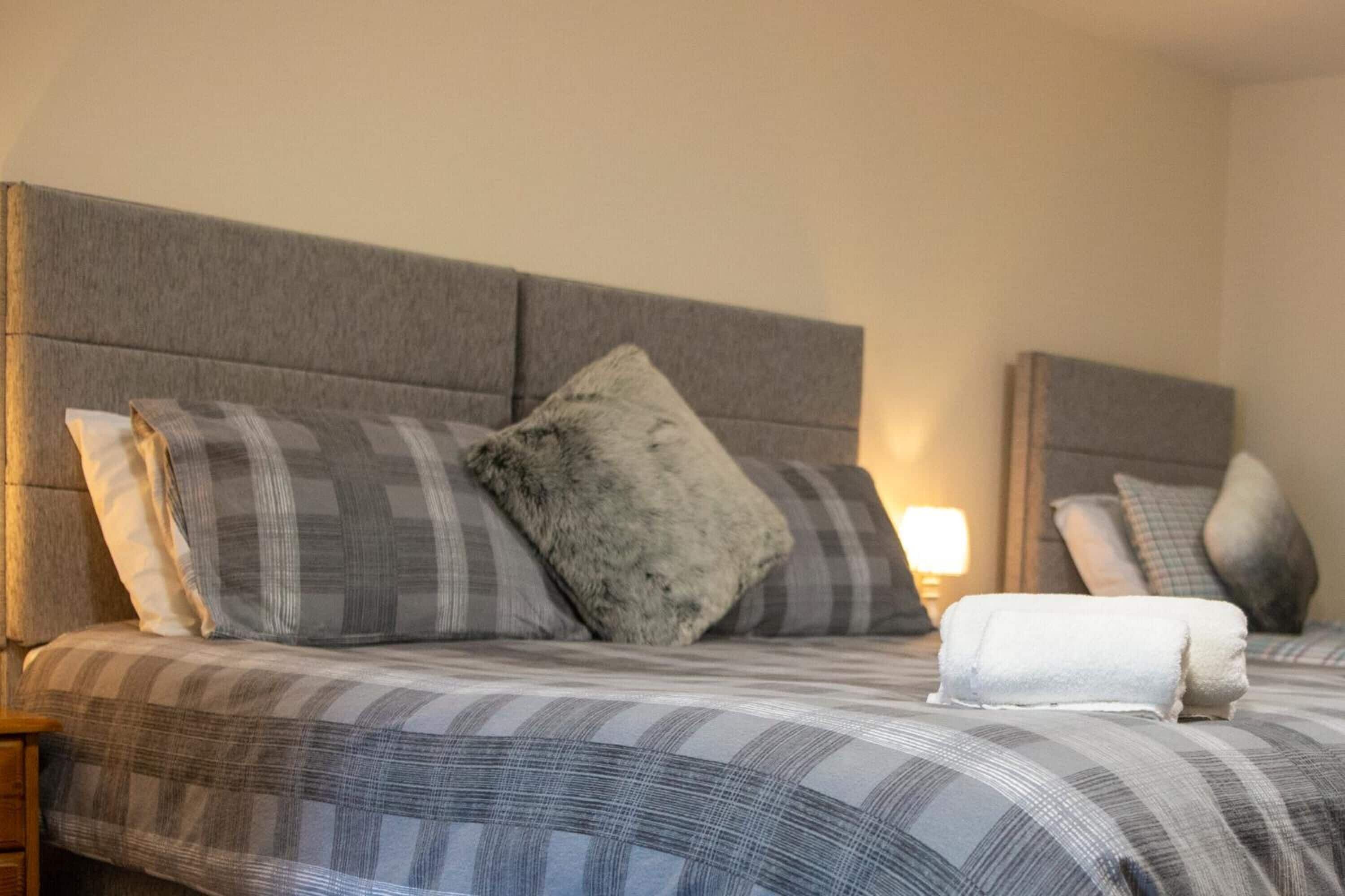A neatly made bed with a grey headboard, grey and white checkered bedding, and a grey fluffy pillow.