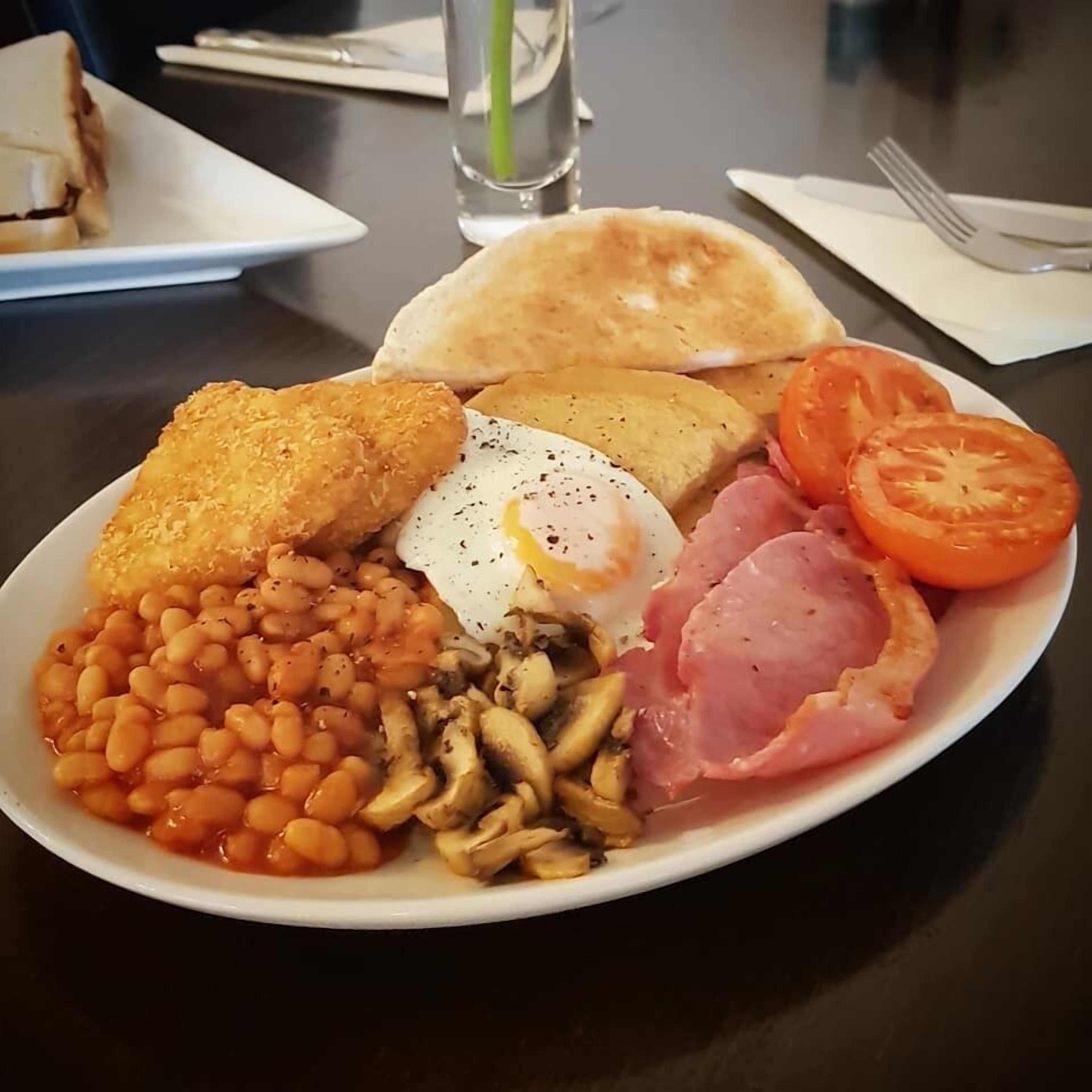 A plate of breakfast food including beans, mushrooms, ham, a fried egg, toast, and a tomato.