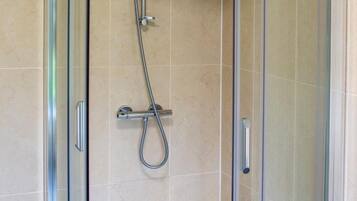 A glass-enclosed shower stall with a handheld showerhead and a wall-mounted faucet.
