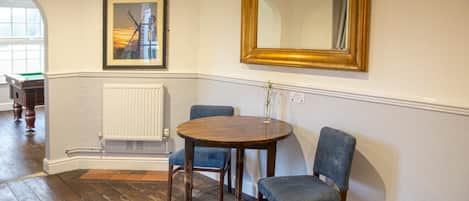 A room with a round wooden table, two blue upholstered chairs, a framed picture, and a large mirror on the wall.
