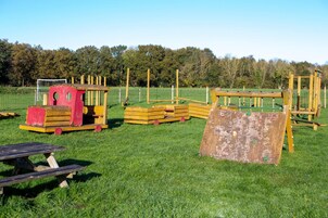 A playground with various play structures, including a slide, climbing frames, and a small building.