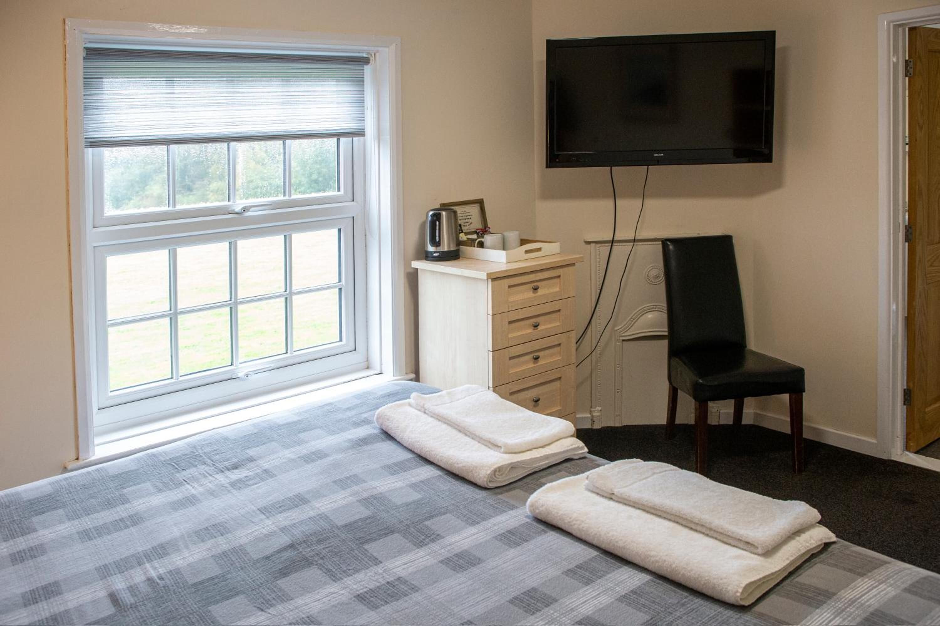 Un dormitorio con cama, televisión, una silla y ventana con persianas.