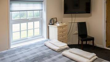 Un dormitorio con cama, televisión, una silla y ventana con persianas.