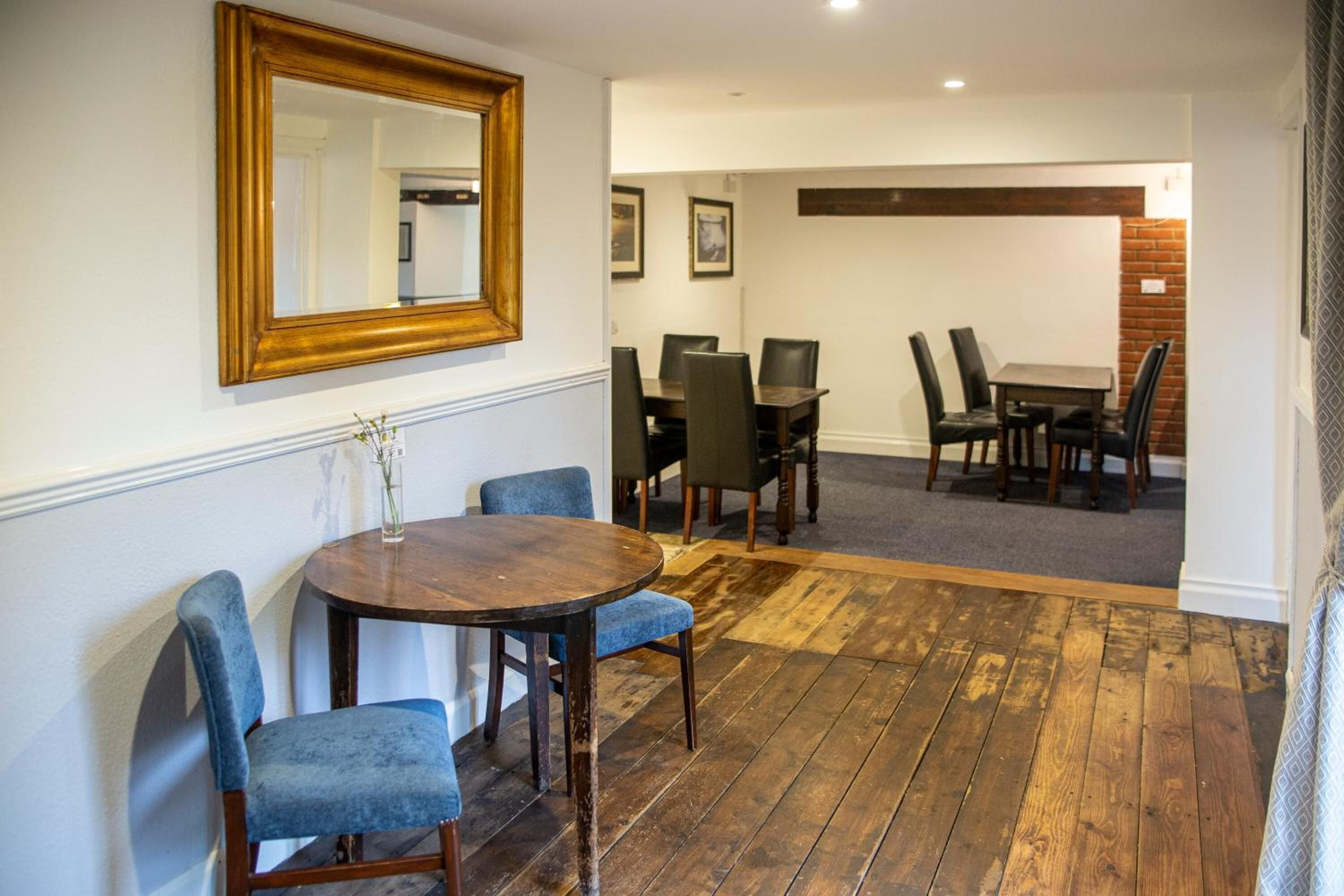A dining area with a wooden table and chairs, a mirror on the wall, and a carpeted floor.