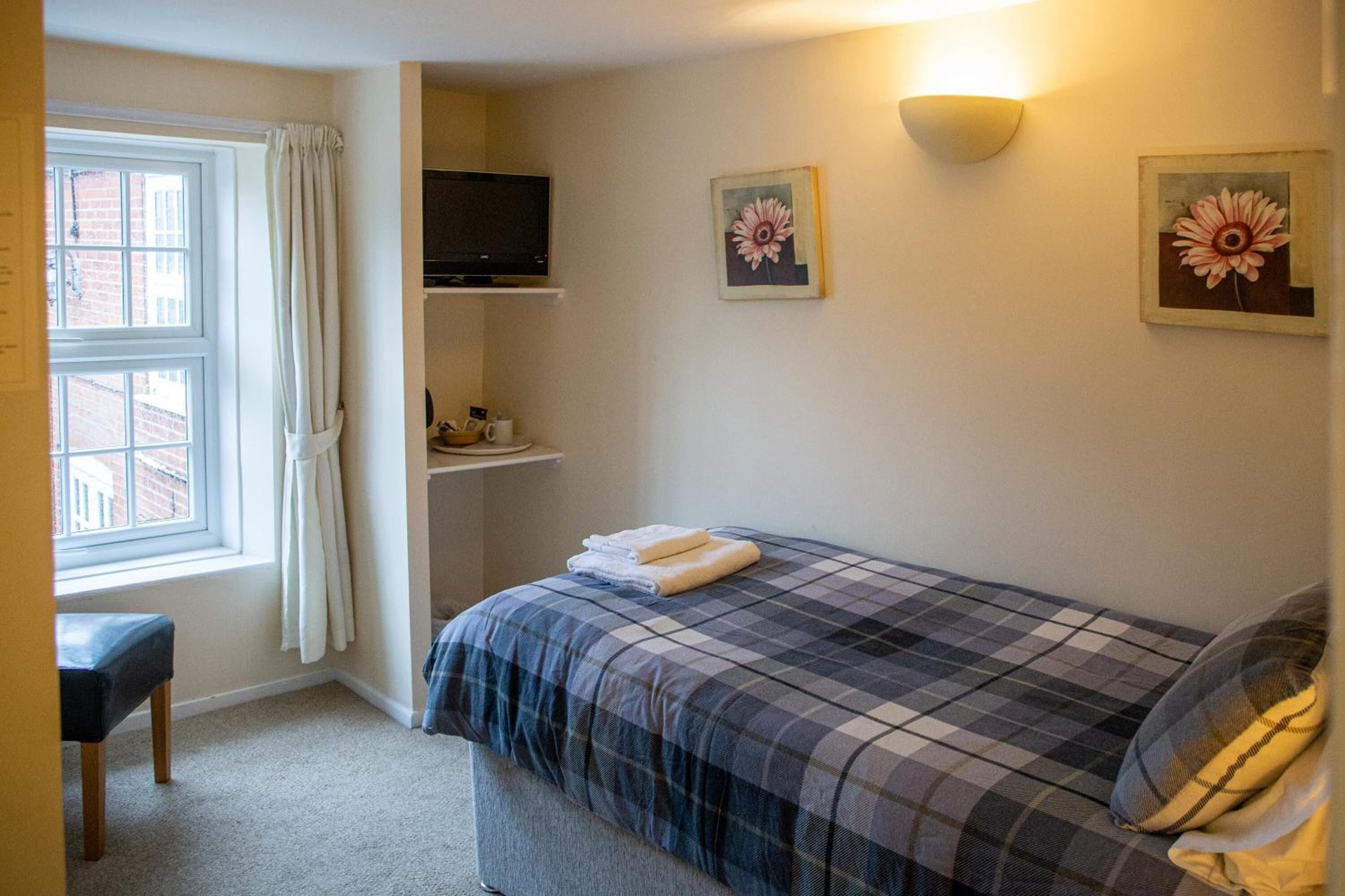 A bedroom with a bed, a television on a shelf, a window with curtains, and two wall-mounted flower paintings.