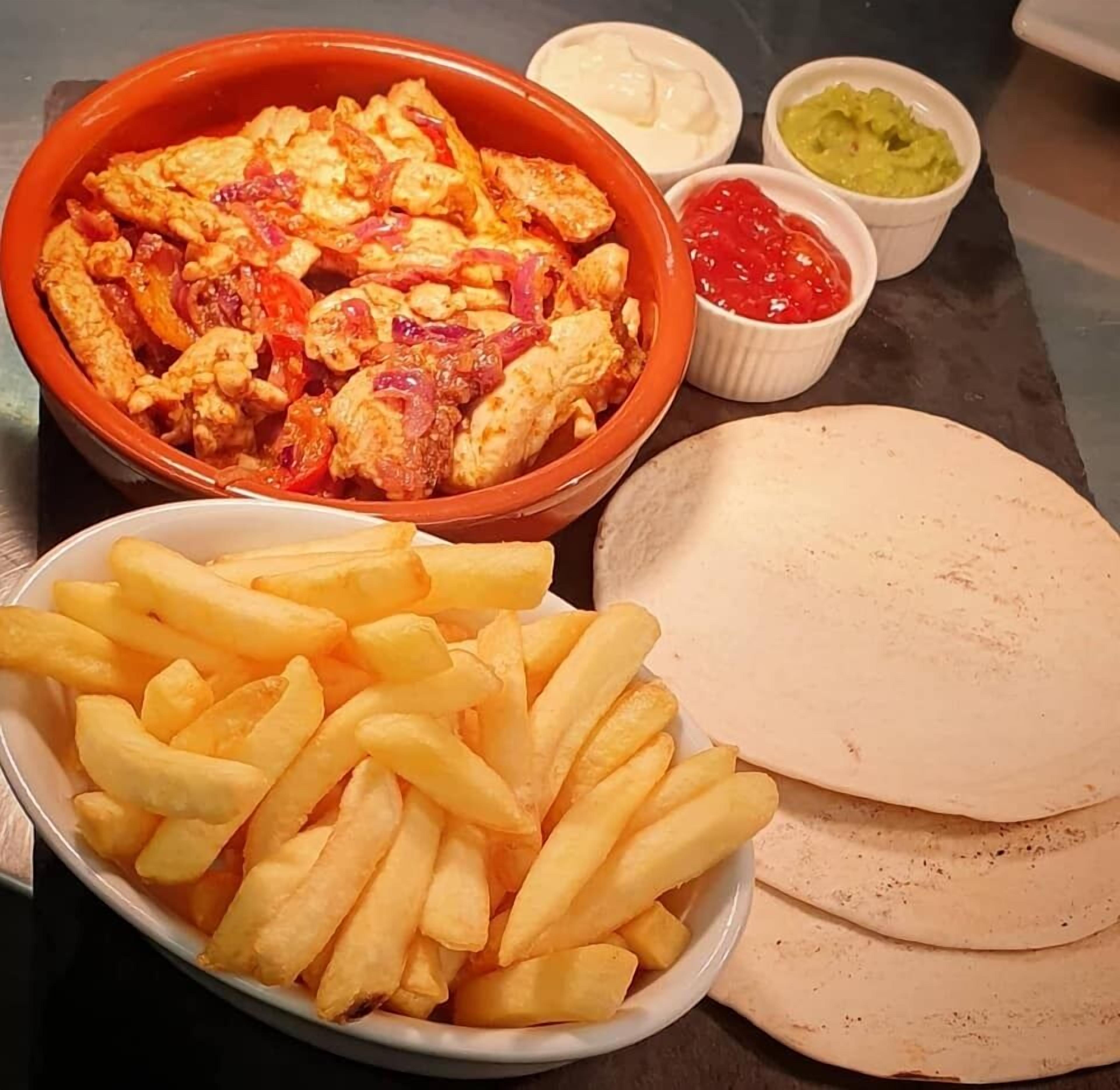 En ret med kylling, pommes frites, tortillas og forskellige saucer.