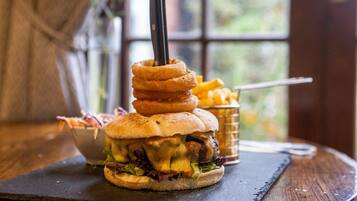 A burger with stacked onion rings and a knife on top, served with fries and a side salad.