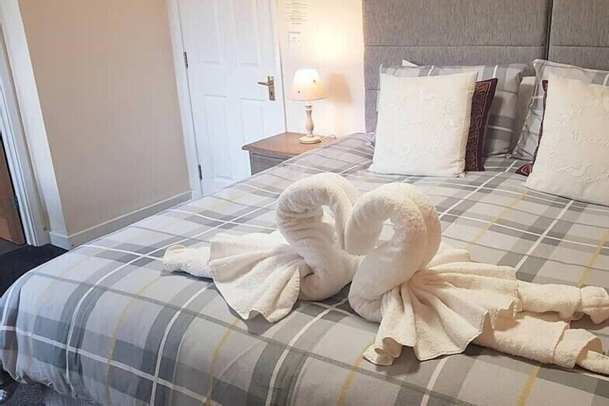 Une chambre d’hôtel avec un lit recouvert d’une courtepointe à carreaux, deux oreillers et une table de chevet avec une lampe.