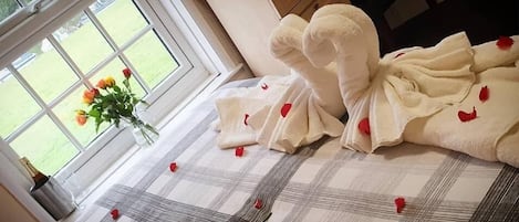 A hotel room with a checkered bedspread, a window with a view of a garden, and a bouquet of flowers on the windowsill.