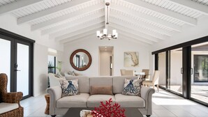 A spacious living room with a high ceiling, a chandelier, a sofa with decorative pillows, a coffee table with a red coral sculpture, and a large window offering a view of the outdoors.