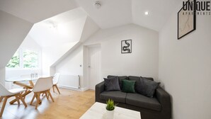 Una sala de estar moderna con una mesa de vidrio, sillas blancas, un sofá gris con cojines y una mesa de centro blanca con una planta.