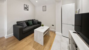Una sala de estar moderna con un sofá gris oscuro, una mesa de centro blanca y un televisor de pantalla plana sobre un mueble blanco.
