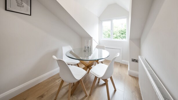 Un comedor moderno con una mesa de vidrio y sillas blancas, una obra de arte enmarcada en la pared, y una ventana con vistas a zonas verdes.