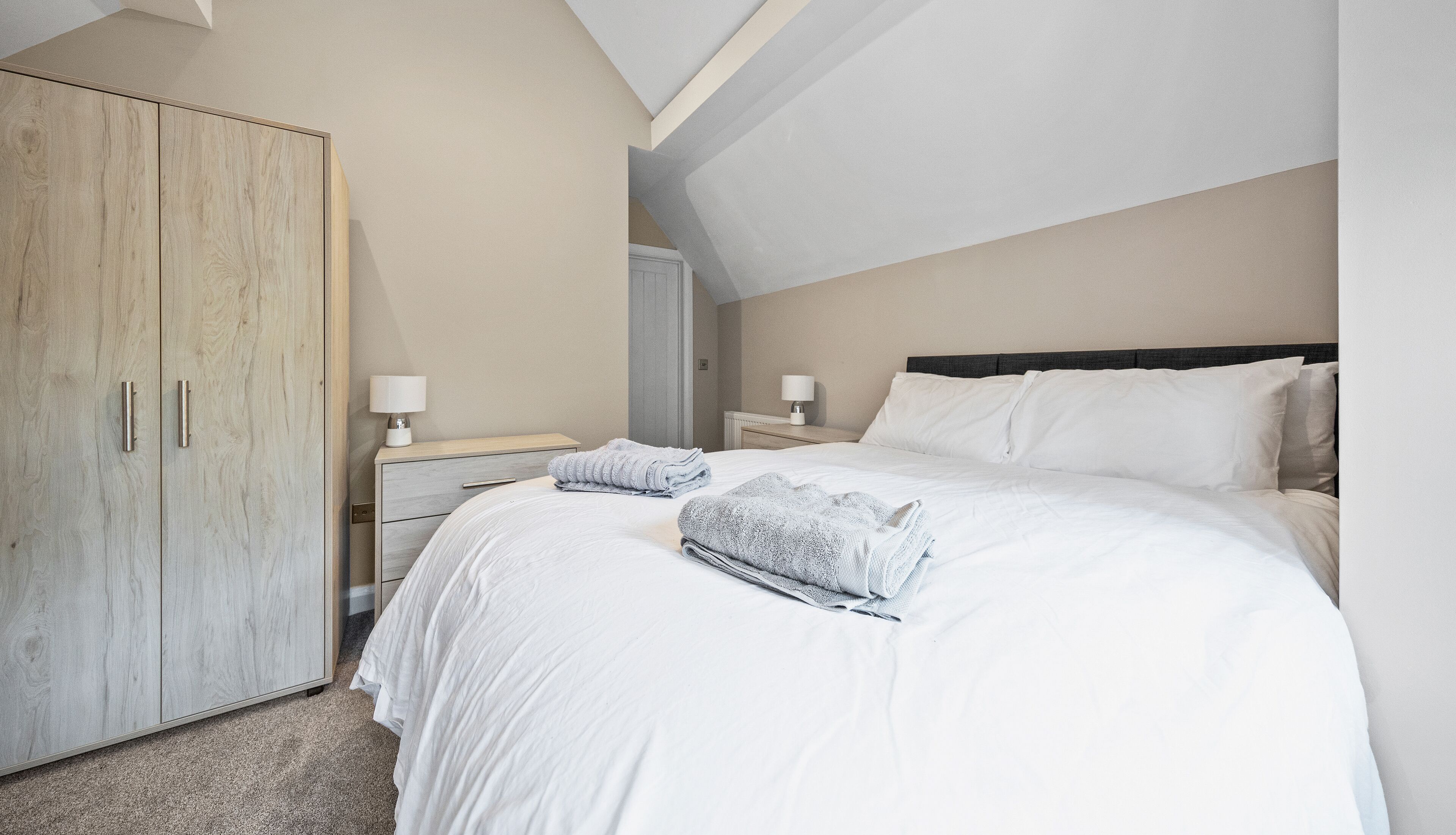 A bedroom with a large bed, a wardrobe, and a nightstand with lamps.