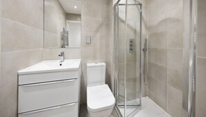 A modern bathroom with a white sink, toilet, and glass shower enclosure. - Stylish 2 Bedroom Apartment (Reading)