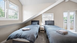 Un dormitorio con dos camas, una mesita de noche, una ventana y una puerta al balcón.