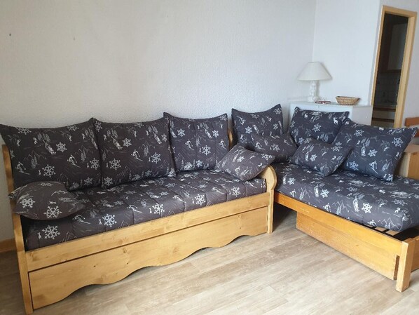Ein Holzsofa mit dunklem gemustertem Stoff, ein kleiner Tisch mit Lampe und ein Spiegel an der Wand.