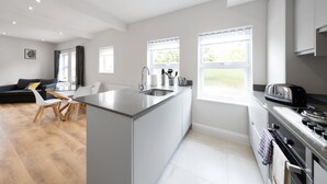 A modern kitchen with a central island, a dining area with a sofa and chairs, and large windows providing natural light. - 2 Bedroom Apartment near Town Center (Reading)