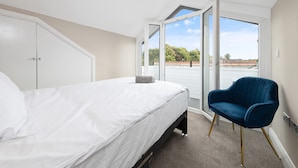A bedroom with a bed, a blue chair, and a large window offering a view of greenery and a building. - 2 Bedroom Apartment near Town Center (Reading)
